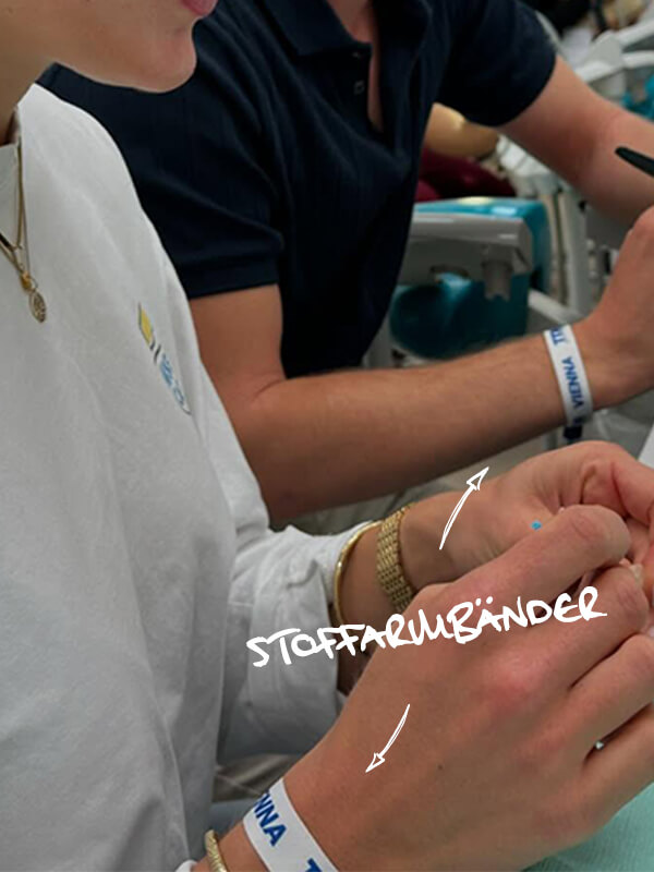 nahaufnahme haende mit stoffarmbaendern mit dem tdm logo drauf